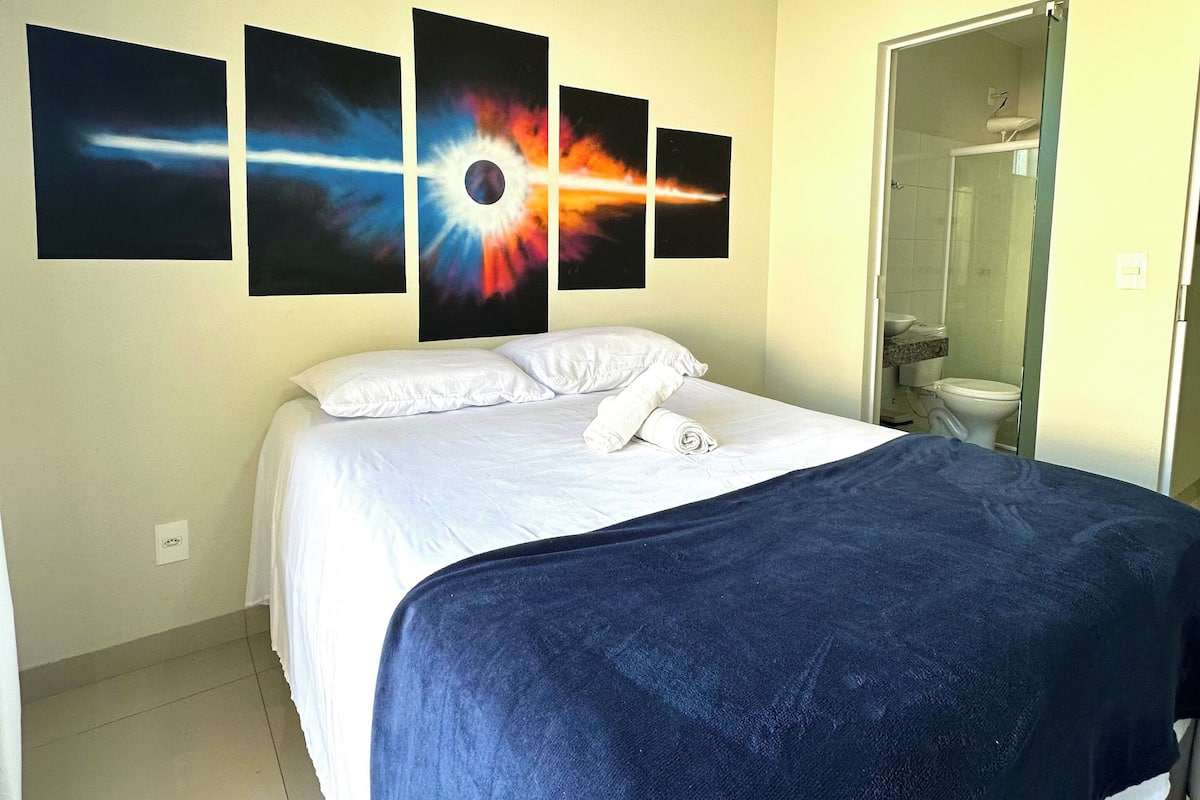 A hotel room with a bed, a shower, and four wall-mounted paintings.