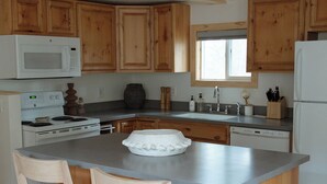 A kitchen with wooden cabinets, a central island with bar stools, a microwave, stove, sink, and a refrigerator. - Mysa Cabin located in a beautiful wooded area outside of Deadwood - 3BR/2B (Lead)