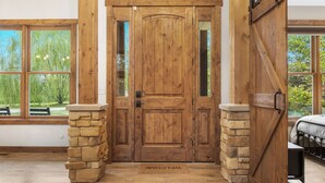 A wooden door with a stone base, flanked by windows with a view of greenery. - Riverfront Chalet on 5 acres~GameRoom~Spa~Gym~Firepit~Theater~2min to CrystalMtn (Thompsonville)