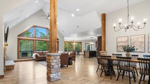 A spacious living area with a high ceiling, large windows, a dining table with chairs, and a fireplace. - Riverfront Chalet on 5 acres~GameRoom~Spa~Gym~Firepit~Theater~2min to CrystalMtn (Thompsonville)