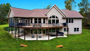 A two-story house with a covered patio, a deck, and a large lawn. - Riverfront Chalet on 5 acres~GameRoom~Spa~Gym~Firepit~Theater~2min to CrystalMtn (Thompsonville)