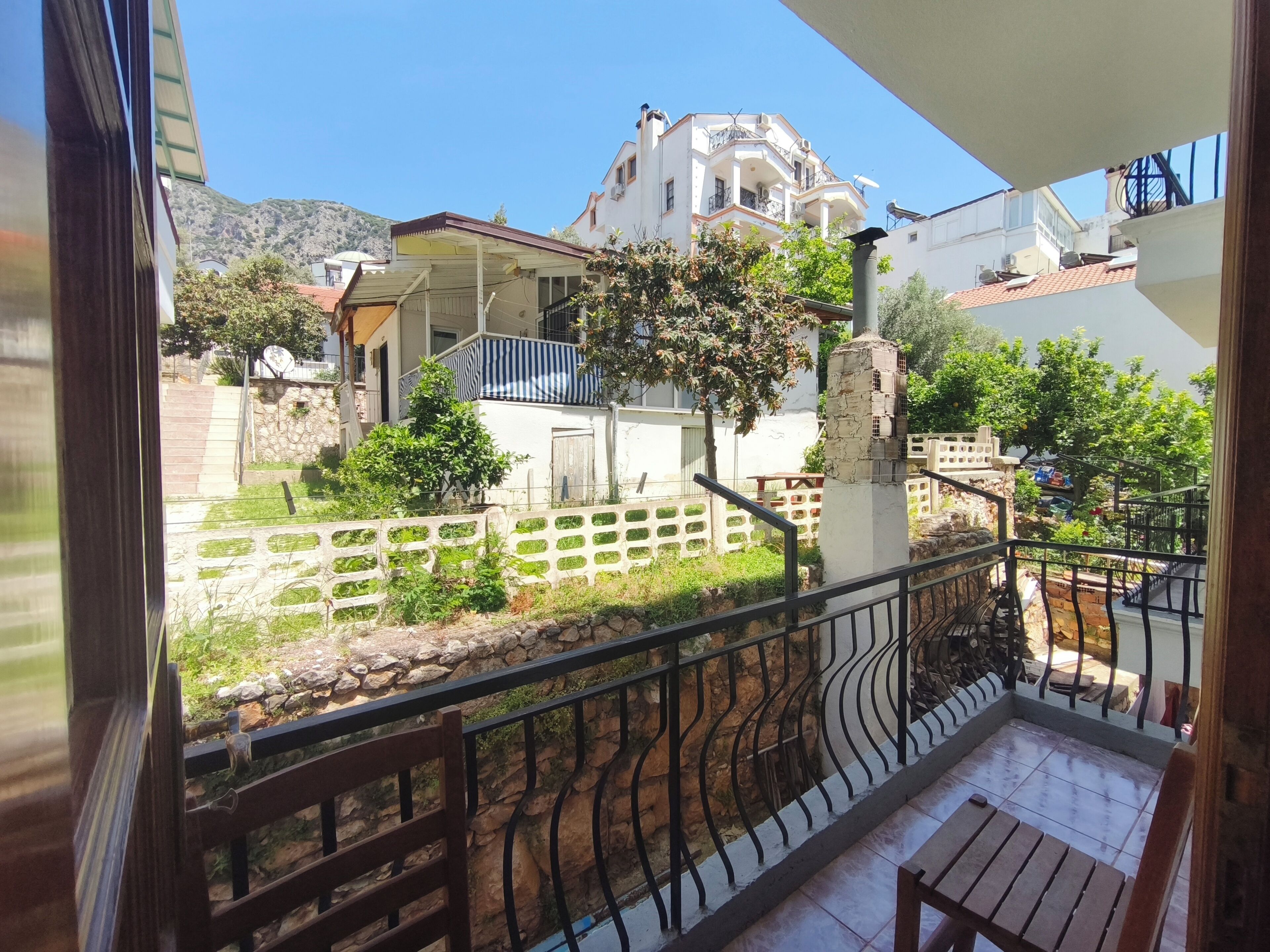 A balcony with a stone wall, a metal railing, and a view of a white building with balconies.