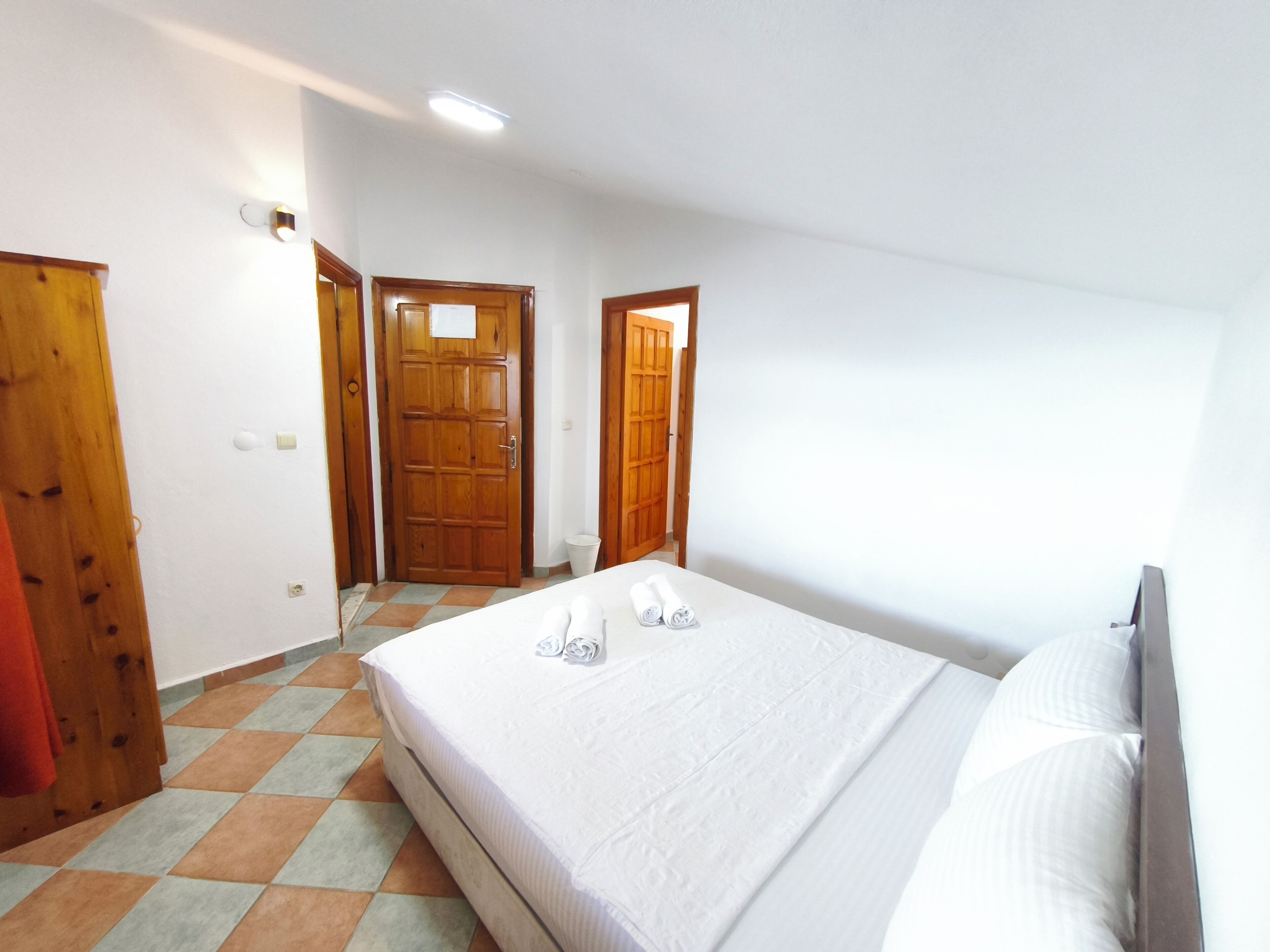 A bedroom with a bed, a wooden door, and a tiled floor.