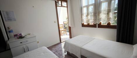 A hotel room with two beds, a desk, a chair, and a window with lace curtains.