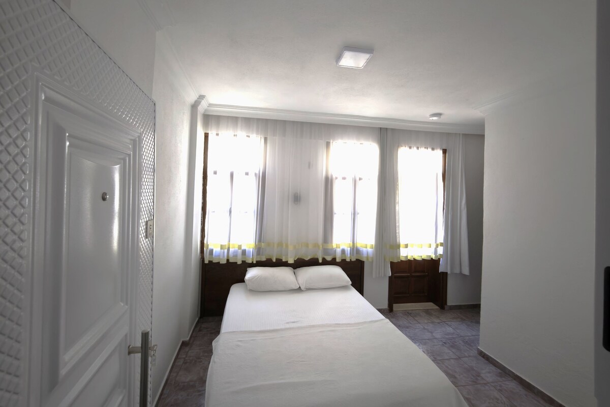 A hotel room with a large bed, a nightstand, a window with curtains, and a door with a textured design.