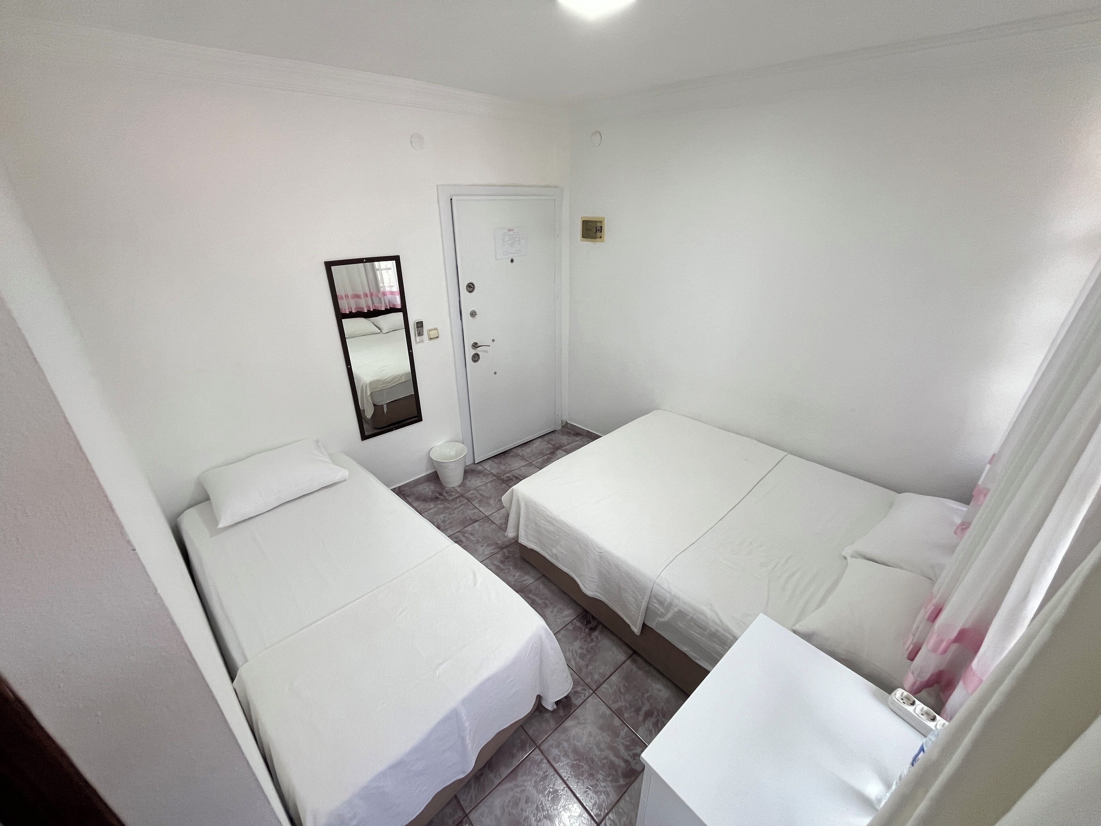 A room with two single beds, a door, a mirror, and a small trash bin.
