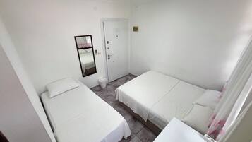 A room with two single beds, a door, a mirror, and a small trash bin.