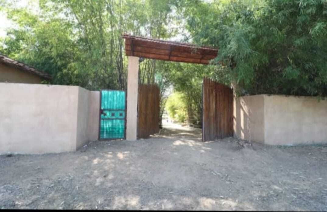 Una entrada con reja y un arco de madera que da a un sendero rodeado de árboles.