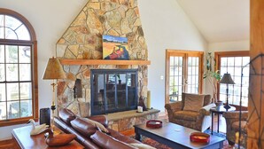 A cozy living room with a stone fireplace, leather sofa, and a painting above it. - A Waterfront Retreat with pier and pool.  Spacious 4 bedrooms near Chestertown. (Chestertown)