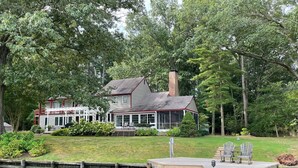 A house with a dock extending into a body of water, surrounded by lush greenery. - A Waterfront Retreat with pier and pool.  Spacious 4 bedrooms near Chestertown. (Chestertown)