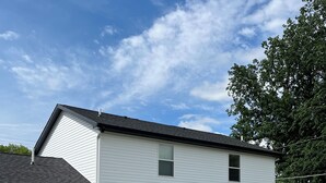 Kaksikerroksinen valkoinen rakennus, jossa on patio, ja patiolla on ulkokalusteita sekä raidallinen aurinkovarjo.