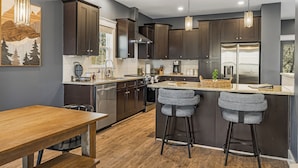 A modern kitchen with dark cabinetry, a wooden dining table, and two bar stools. - Forest Mountain Views with Yard, 3-bedroom pet friendly home Fairview (Fairview)