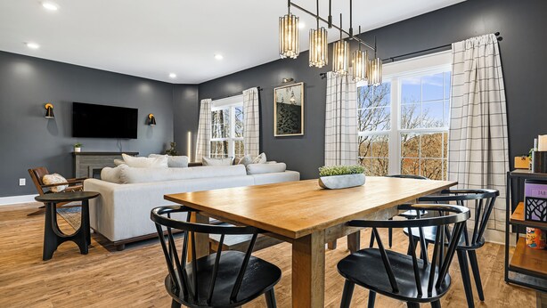 A modern living room with a sofa, dining table, and chairs, a flat-screen TV, and a large window with curtains. - Forest Mountain Views with Yard, 3-bedroom pet friendly home Fairview (Fairview)