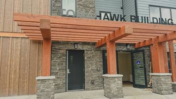 A building entrance with a wooden pergola, stone pillars, and a sign reading "TO HAWK BUILDING".