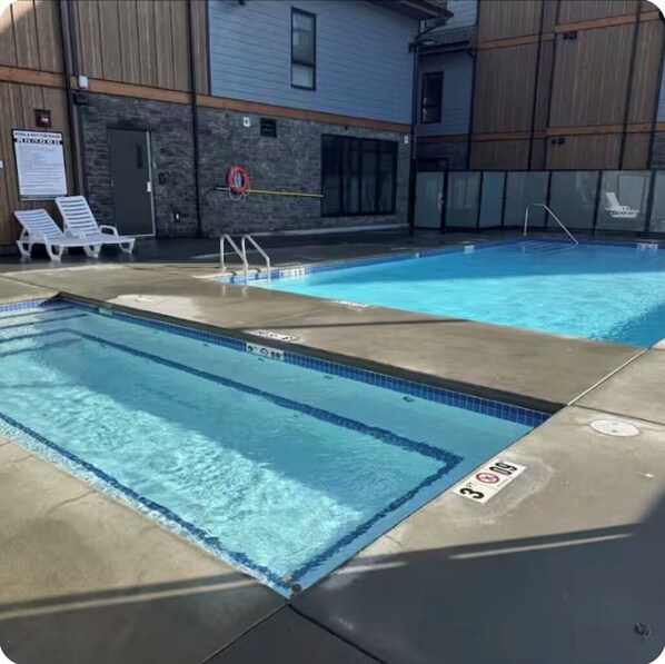A swimming pool with two separate sections, lounge chairs, and a building with a stone facade in the background. - Stunning 2-Bedroom Condo with Breathtaking Mountain Views (Dead Man's Flats)