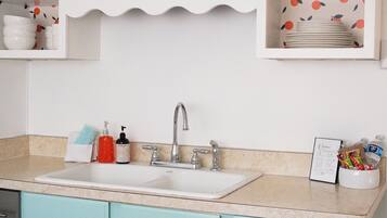A kitchen with white upper cabinets, a teal lower cabinet, a sink with a faucet, and a countertop with various items.