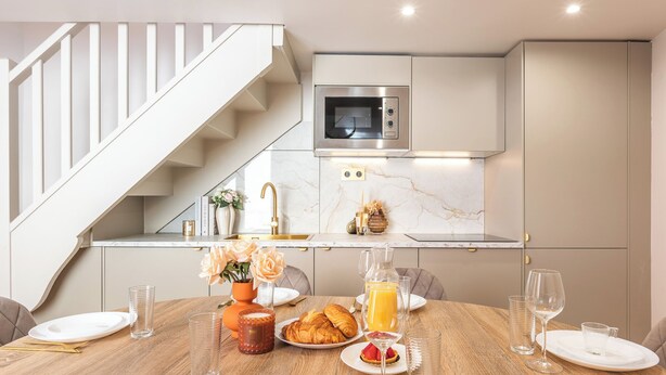 A modern kitchen with a built-in microwave, a wooden dining table set with plates, glasses, and a croissant. - Refined Apartment with Jacuzzi and AC - 6P PARIS 10 minutes République Bastille (Paris)