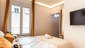 A hotel room with a bed, a TV, a window with curtains, and a view of the outside balcony. - Refined Apartment with Jacuzzi and AC - 6P PARIS 10 minutes République Bastille (Paris)