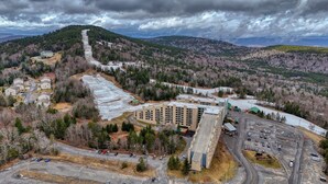 An aerial view of a residential area with a large building, multiple parking lots, and surrounding forested hills. - Ski Paradise (Snowshoe)