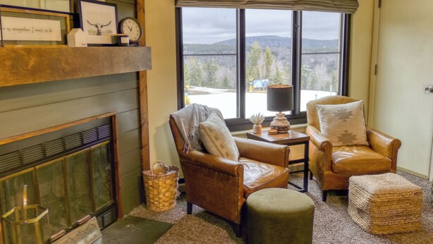 A cozy living room with a fireplace, leather armchairs, a coffee table, and a large window offering a view of the outdoors. - Ski Paradise (Snowshoe)