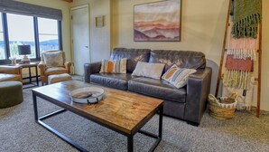 A living room with a leather sofa, a wooden coffee table, and a large window. - Ski Paradise (Snowshoe)
