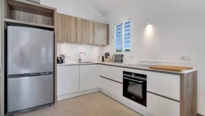 Une cuisine moderne avec des meubles blancs, un réfrigérateur en acier inoxydable, un four encastré et une fenêtre équipée de stores.