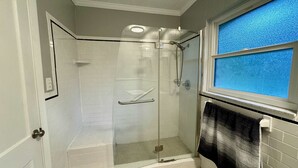 A shower with a glass door, a handrail, and a window with a blue view. - the nest (Gainesville)