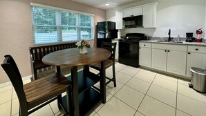 A kitchen with white cabinets, a black stove, and a microwave. There is a dining table with chairs and a vase with flowers. - the nest (Gainesville)
