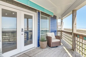 A covered porch with a wicker chair, a potted plant, and a view of the beach. - Gulf-View Deck: West End Family Home in Galveston! (Galveston)