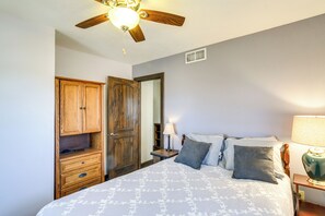 Un dormitorio con cama, armario de madera, mesita de noche, lámpara y ventilador de techo.