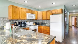 A kitchen with wooden cabinets, a microwave, stove, sink, and a refrigerator. - Riverfront Cabin Near Dtwn Pella w/ Game Room! (Pella)