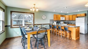 A kitchen with wooden cabinets, a dining table with chairs, a large window, and a clock on the wall. - Riverfront Cabin Near Dtwn Pella w/ Game Room! (Pella)