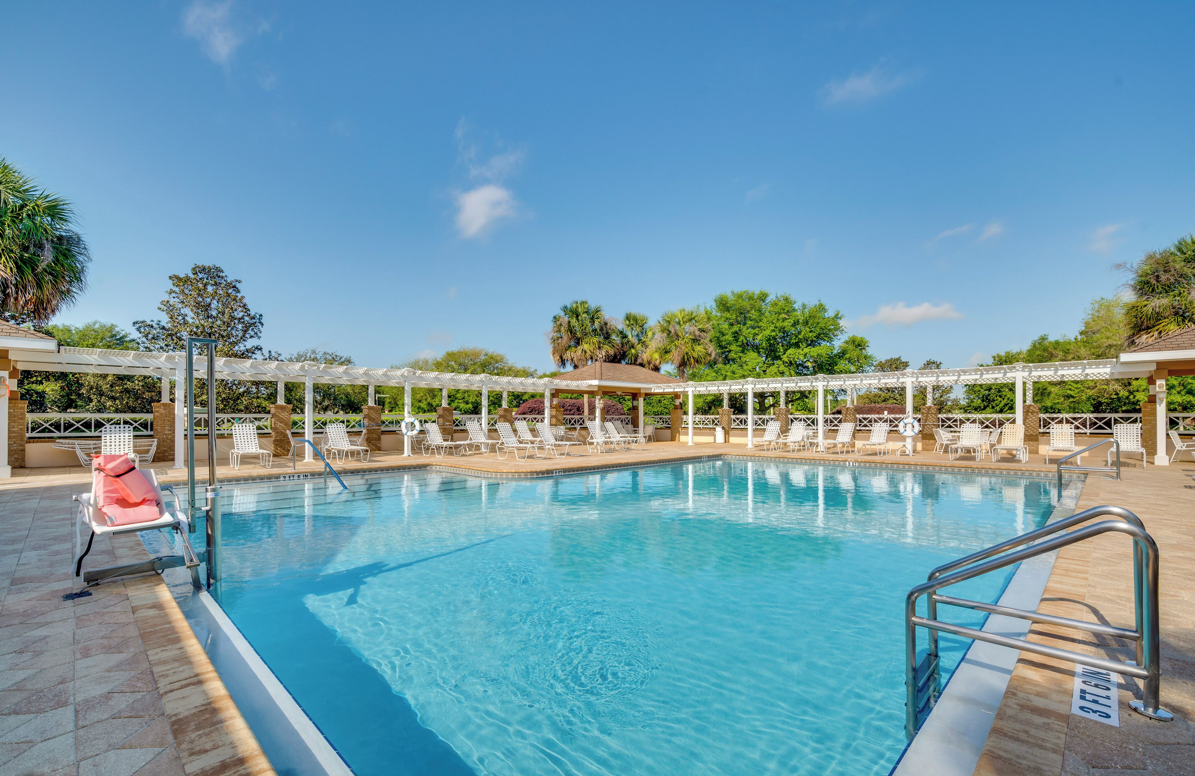 En klarblå pool med vita solstolar och ett avskärmat område.