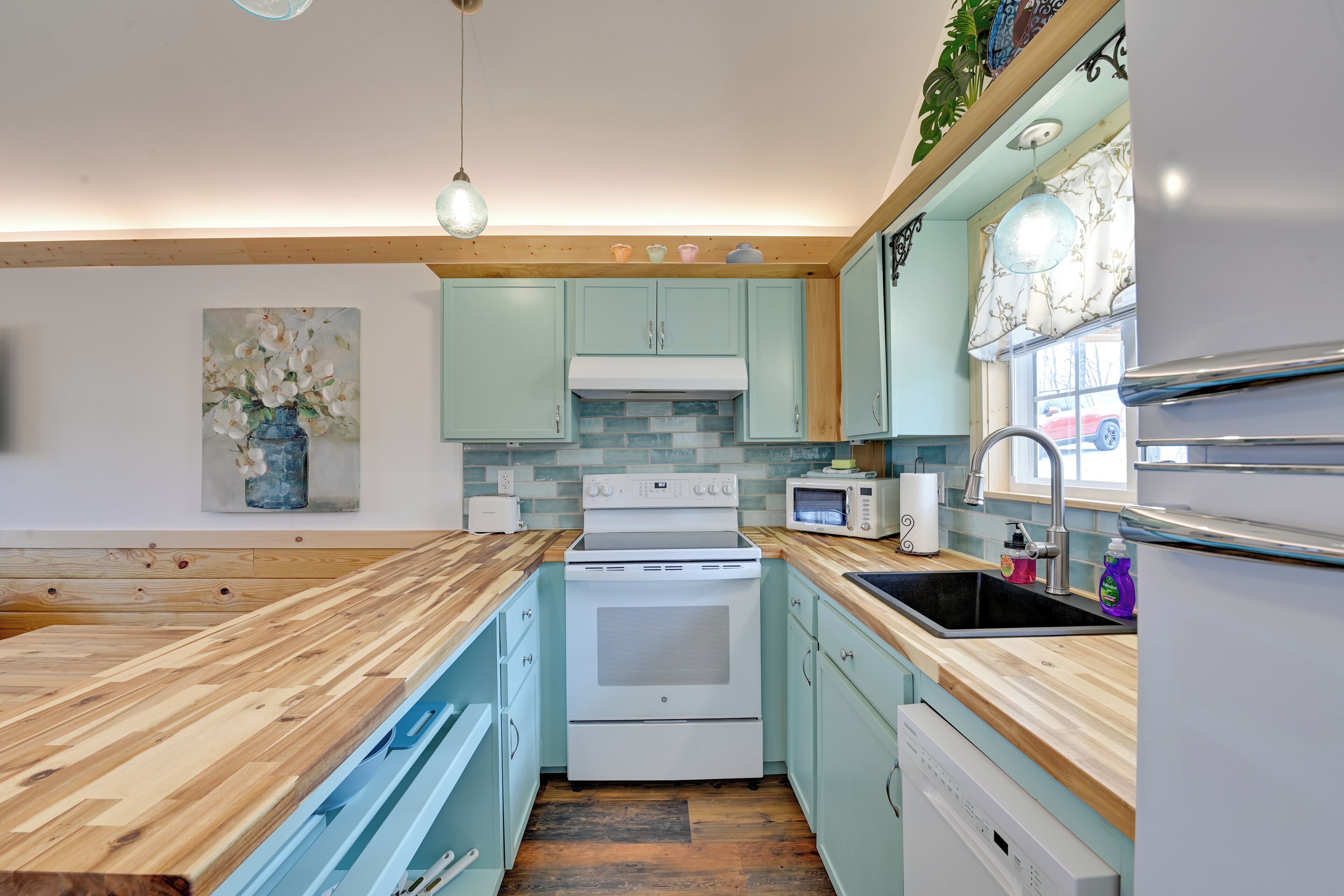 A kitchen with light blue cabinets, a wooden countertop, a white stove, a microwave, and a sink.