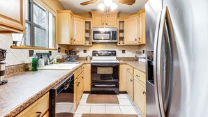A kitchen with wooden cabinets, a stainless steel refrigerator, a microwave, and a ceiling fan. - 3 Mi to Dtwn New Haven: Colorful Condo w/ Yard! (East Haven)