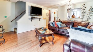 A living room with a wooden floor, a leather sofa, a glass coffee table, and a flat-screen TV mounted on the wall. - 3 Mi to Dtwn New Haven: Colorful Condo w/ Yard! (East Haven)