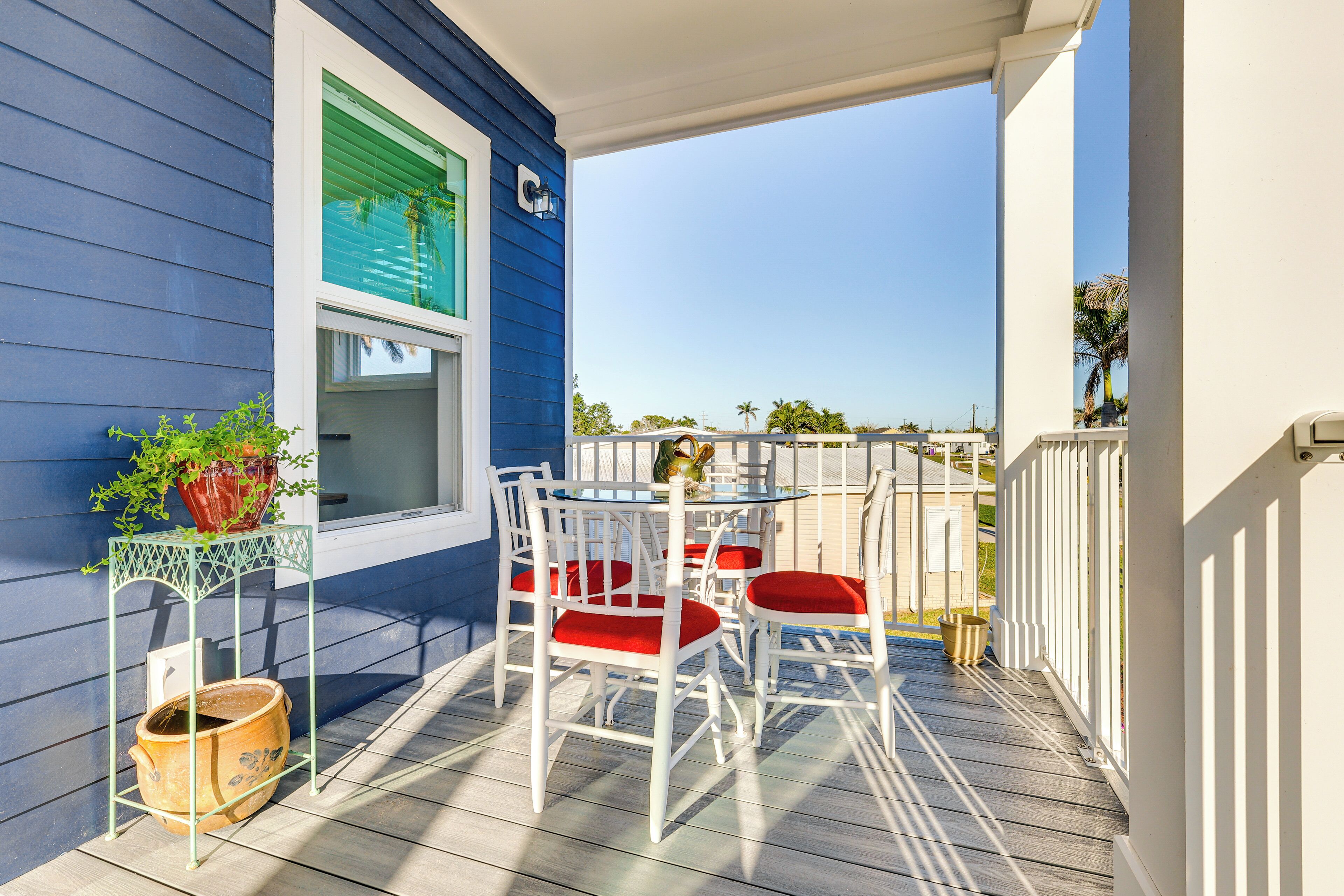 Een balkon met een witte tafel en stoelen, een plant in pot en een raam met groene luiken.