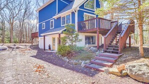 Une maison à deux étages, avec une façade bleue, un porche à l’avant et un escalier en bois menant à un balcon.
