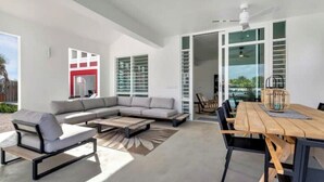 A modern living room with a sectional sofa, a dining table with chairs, and a large window with blinds. - Waterdream Villa, Water Villas (Kralendijk)