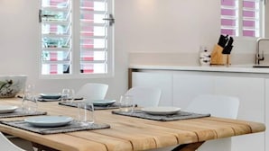 A modern dining area with a wooden table set for four, white chairs, and a kitchen counter with utensils. - Waterdream Villa, Water Villas (Kralendijk)