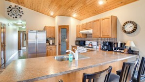 A kitchen with wooden cabinets, a stainless steel refrigerator, a microwave, and a clock on the wall. - 6 Mi to Dtwn Pella: Riverfront Cabin w/ Game Room! (Pella)