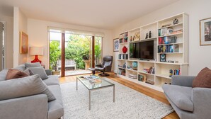 Ein modernes Wohnzimmer mit grauen Sofas, einem Glastisch, einem Ledersessel und einem Bücherregal mit Büchern und Dekoration.