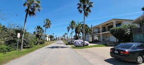 A residential street with palm trees, a covered car, and a building with balconies. - * Bay View  Great Deck *2 levels  & 3 bedr * Pool (South Padre Island)
