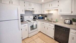 A modern kitchen with white cabinets, a stove, microwave, toaster, and dishwasher.
