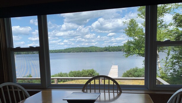 Un comedor con mesa y sillas, un cuaderno y vistas a un lago con árboles y un muelle.