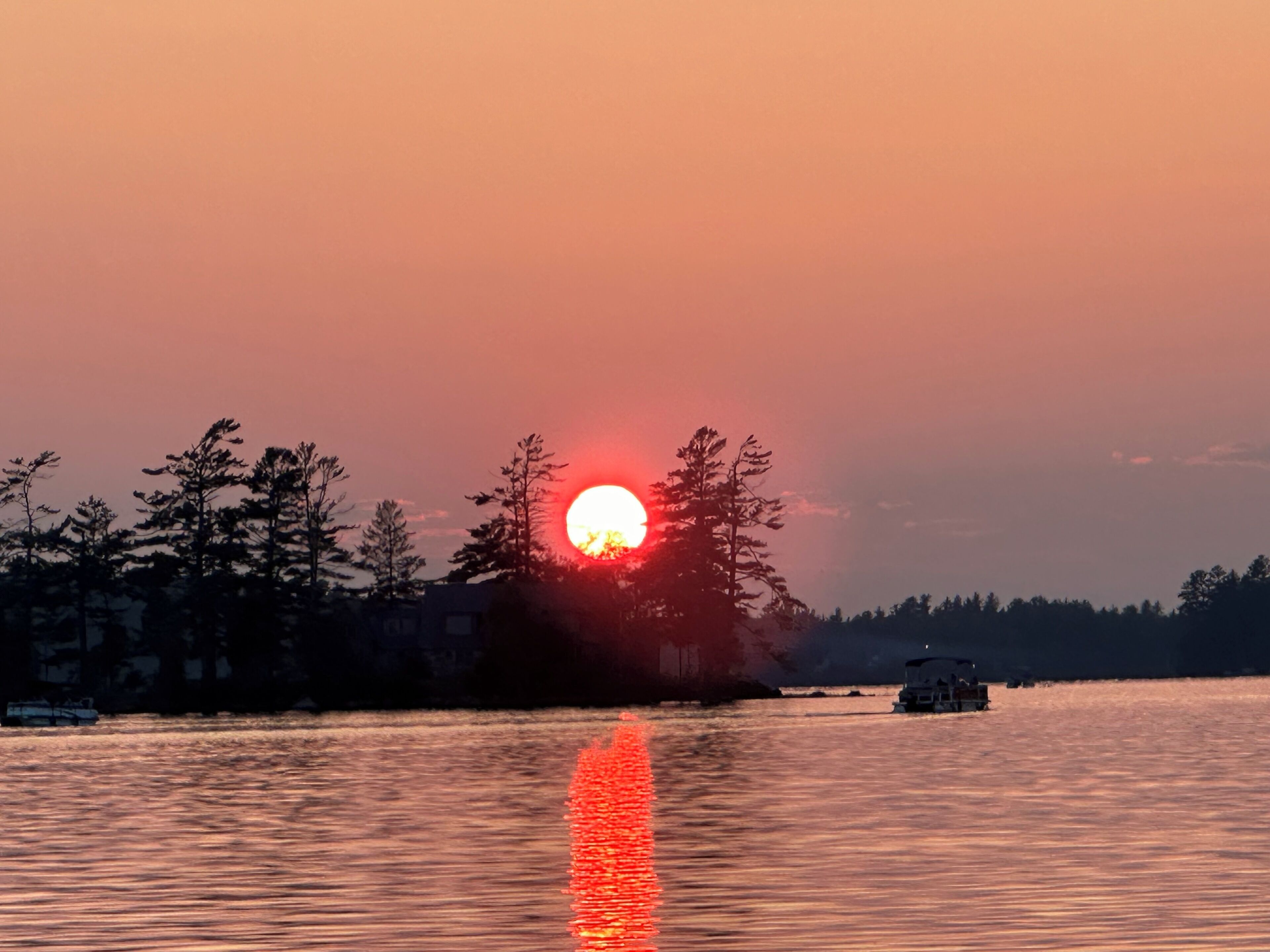 Ein Sonnenuntergang über ruhigem Gewässer, ein Boot ist in der Ferne zu sehen.
