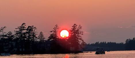 Ein Sonnenuntergang über ruhigem Gewässer, ein Boot ist in der Ferne zu sehen.