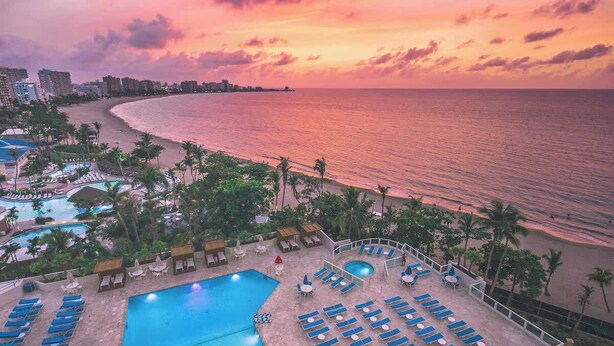A resort with multiple swimming pools, sun loungers, and a beach view.