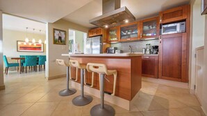 A modern kitchen with wooden cabinets, a stainless steel refrigerator, a microwave, and a central island with bar stools.