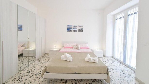 A bedroom with a bed, bedside tables, a large mirror, and a window with curtains. - Casa Lulù (Ischia)